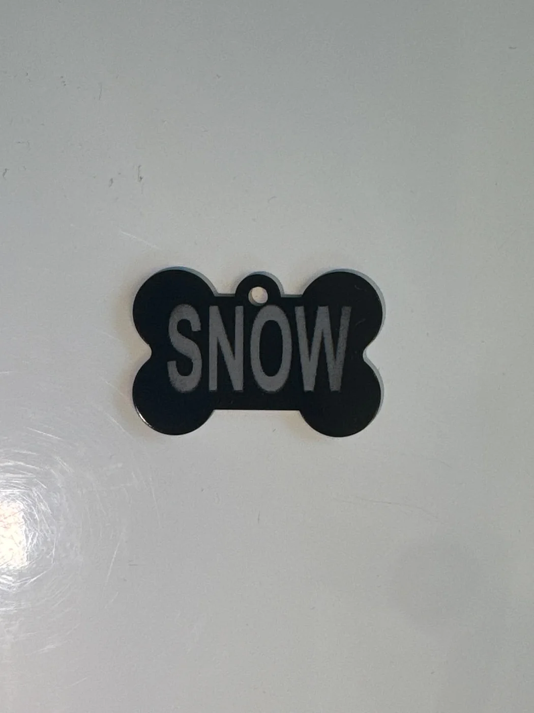 Black bone-shaped pet tag engraved with the name Snow